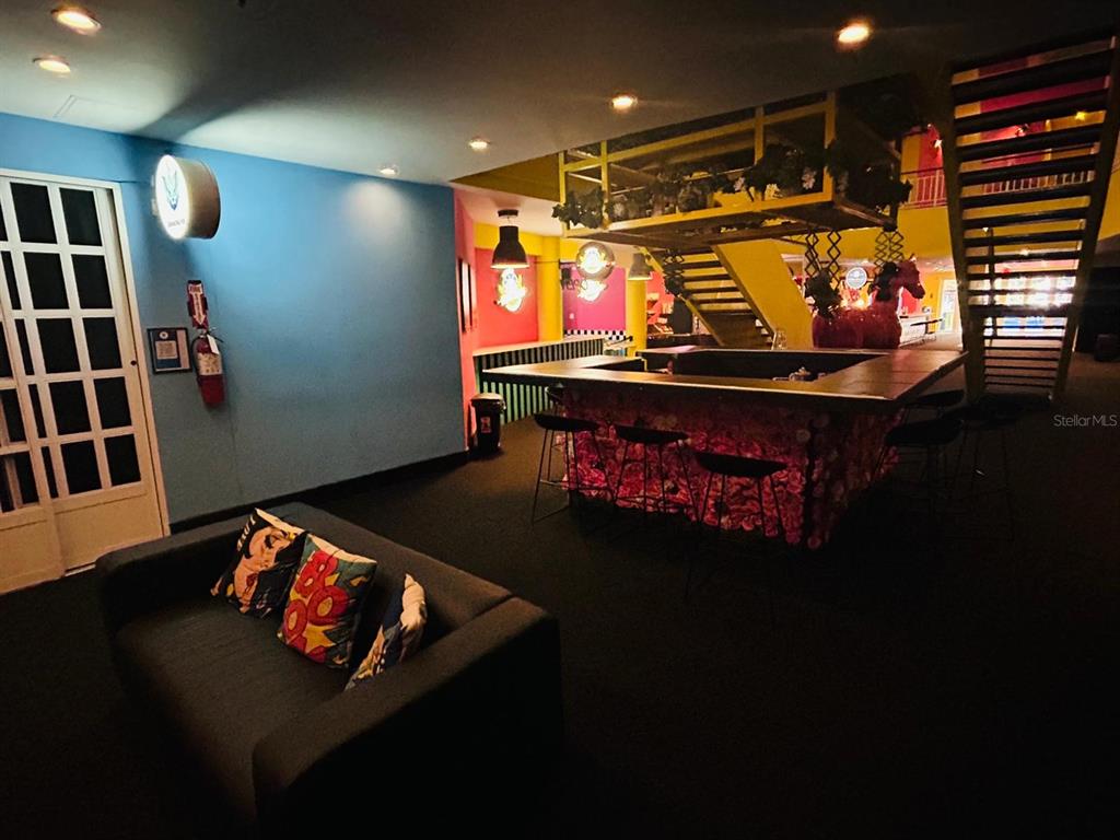 A lounge area features a dark sofa, a floral-covered bar, and a yellow staircase — C. Isabel-Muñoz Rivera C. ISABEL-MUÑOZ RIVERA, PONCE, PR