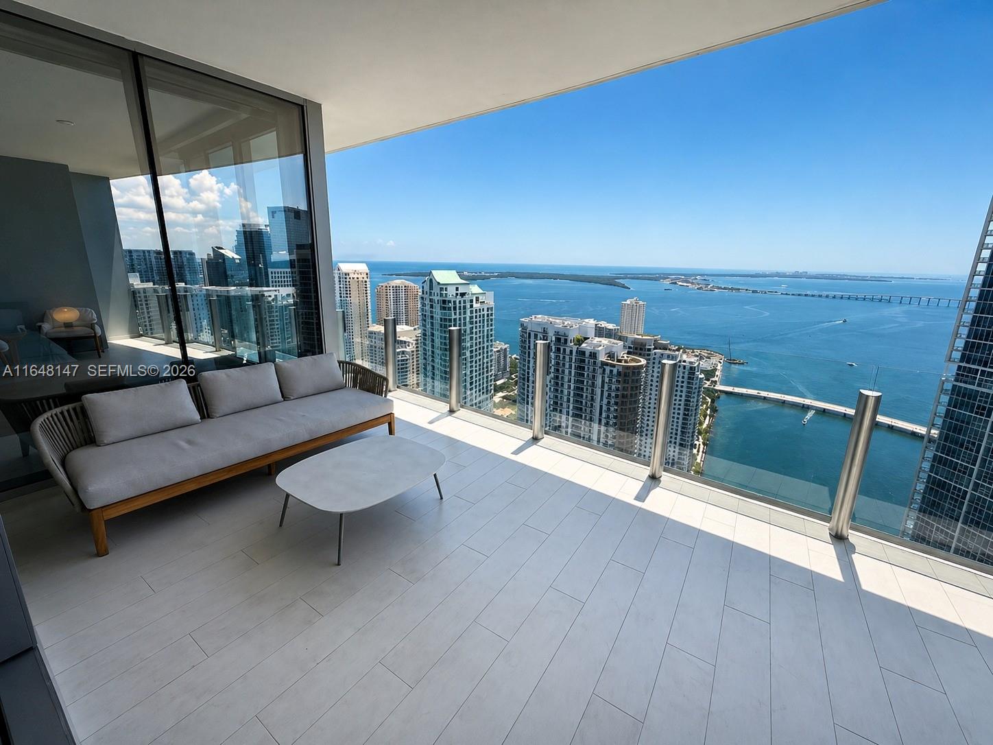 A high-rise balcony features a modern sofa, a coffee table, and panoramic ocean views — 300 Biscayne Blvd Way # 4604, Miami FL 33131, MIAMI, FL