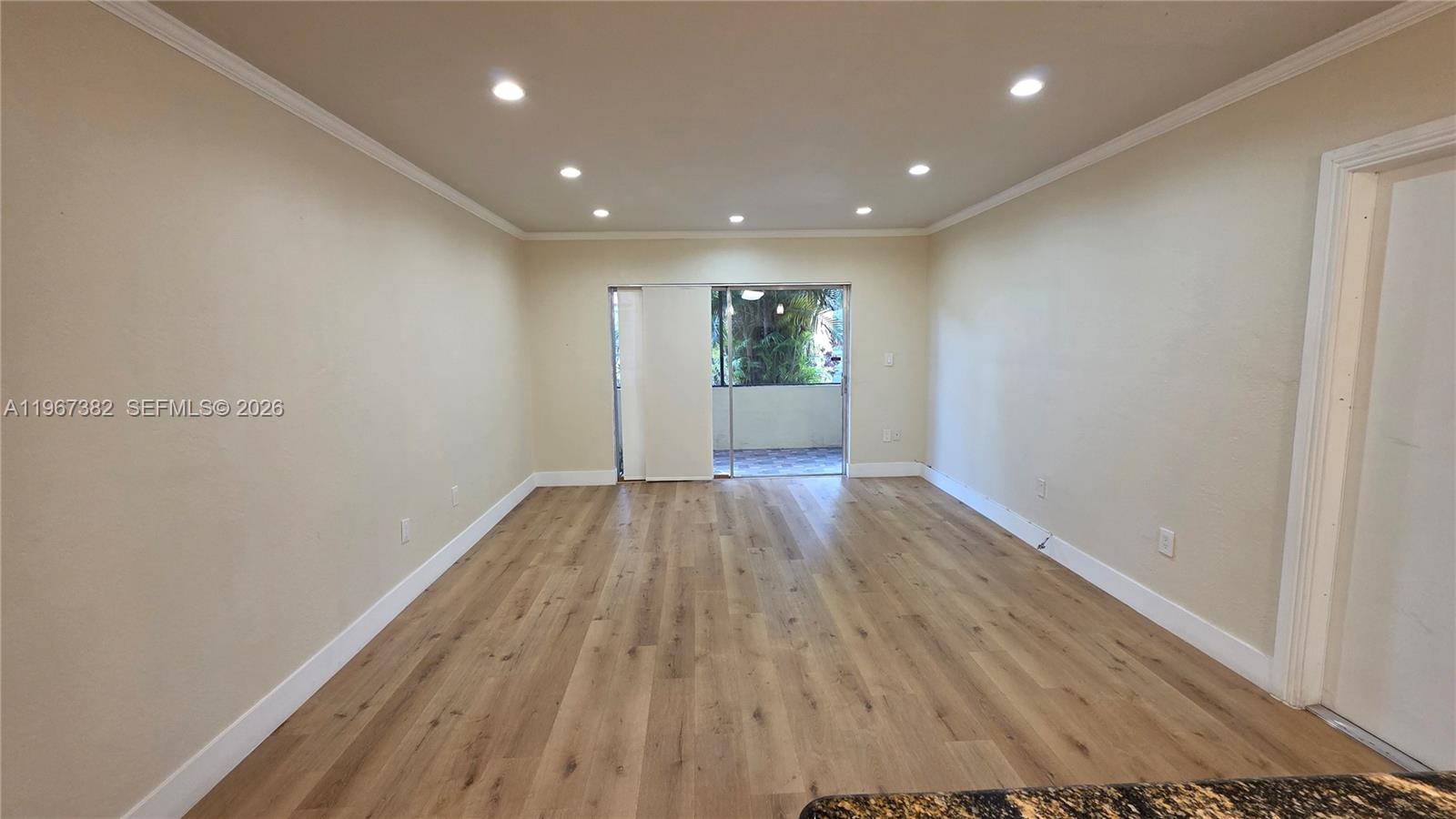 An empty room features light-colored walls, recessed ceiling lights, and wood-look flooring leading to a balcony — 7829 Miller Dr # B104, Miami FL 33155, MIAMI, FL