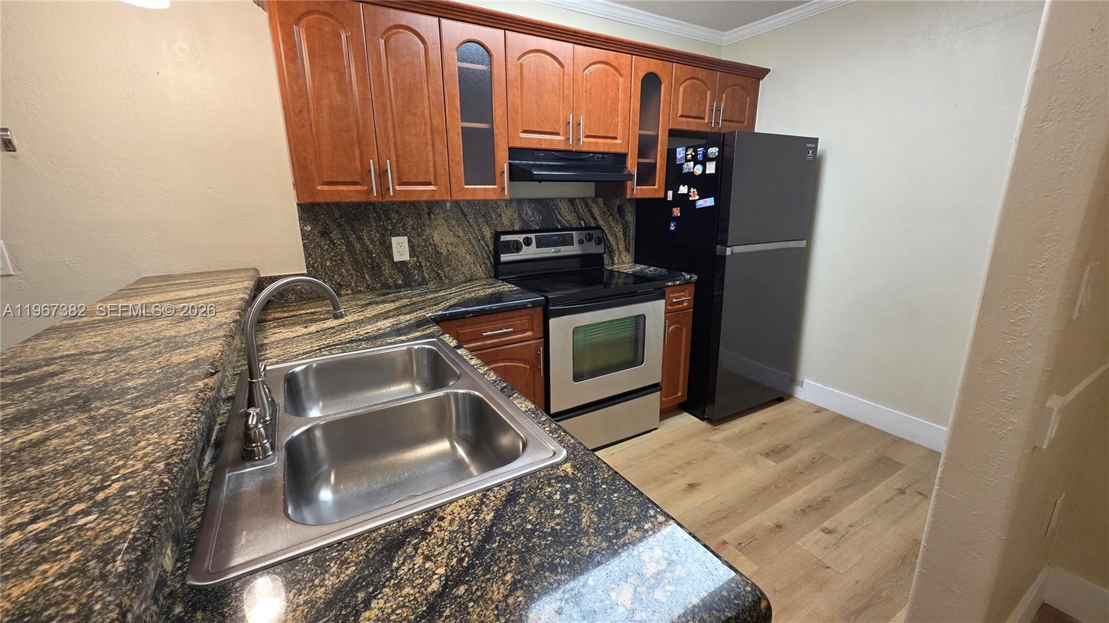 A kitchen features wood cabinets, dark granite countertops, stainless steel appliances, and wood-look flooring — 7829 Miller Dr # B104, Miami FL 33155, MIAMI, FL