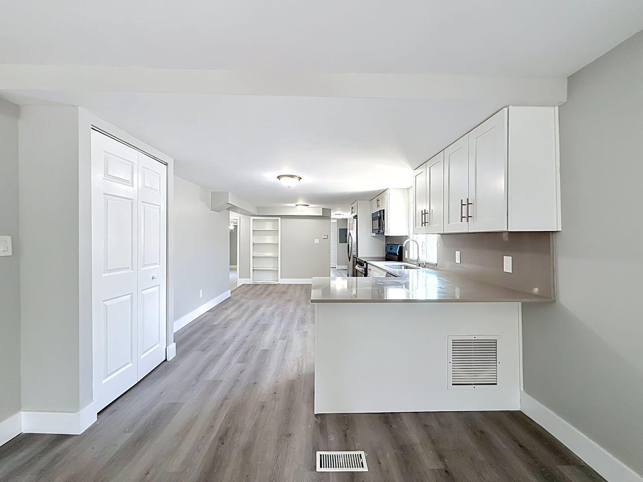 A kitchen with white cabinets and a peninsula opens into a living area with flooring — 2611 E Marina Drive, Dania Beach FL 33312, DANIA BEACH, FL