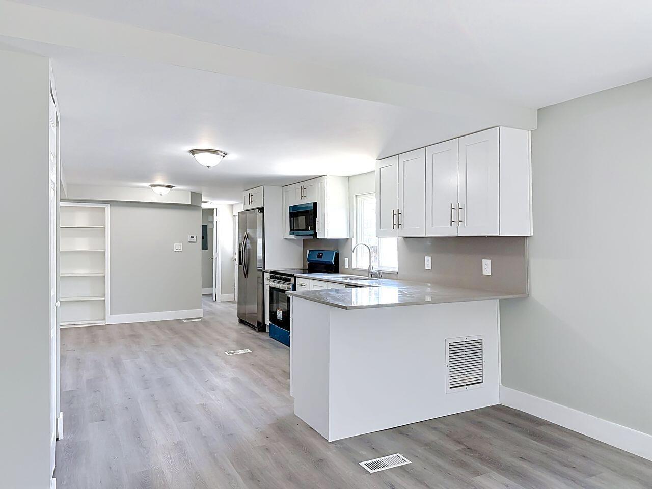 A kitchen with white cabinets, stainless steel appliances, and gray countertops opens to a living area — 2611 E Marina Drive, Dania Beach FL 33312, DANIA BEACH, FL