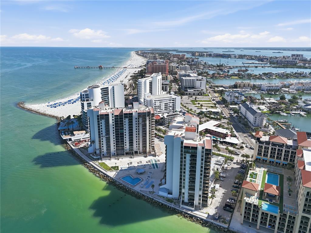 An aerial view shows high-rise beachfront condominiums along a coastline with a pier and water — 450 S GULFVIEW BOULEVARD UNIT 301, CLEARWATER BEACH, FL