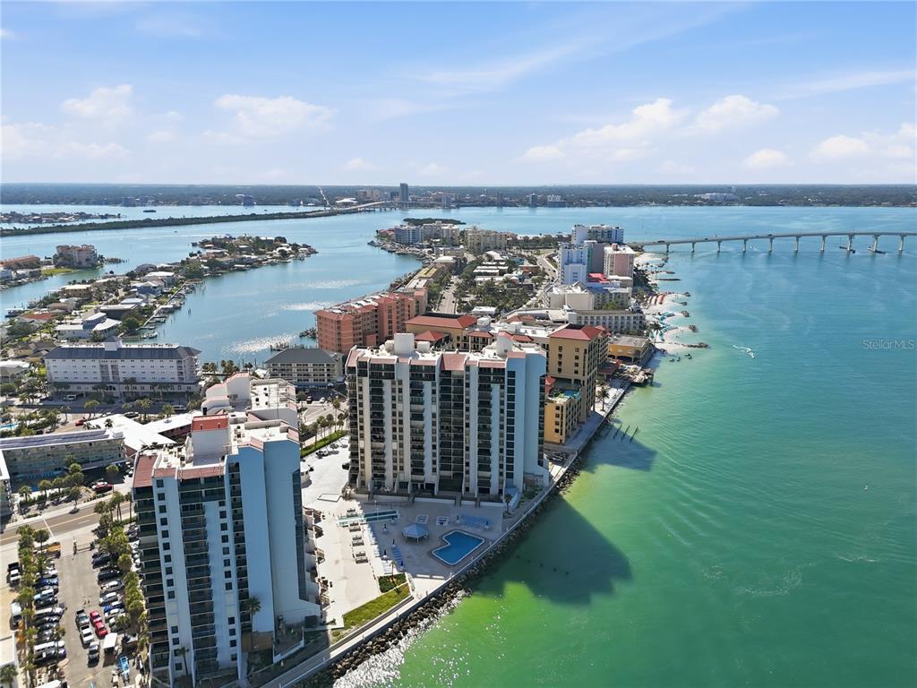An aerial view shows high-rise condominiums along a coastline with a bridge in the background — 450 S GULFVIEW BOULEVARD UNIT 301, CLEARWATER BEACH, FL