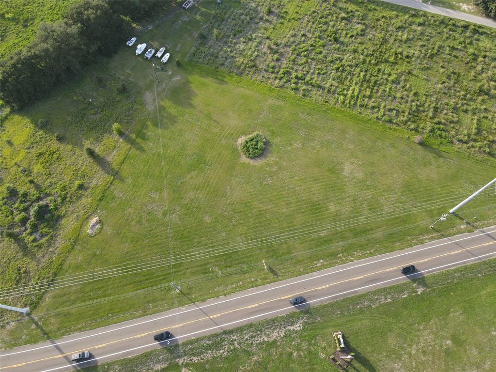 An aerial view shows a grassy, triangular plot of land adjacent to a paved road — 104 SCENIC HIGHWAY, HAINES CITY, FL