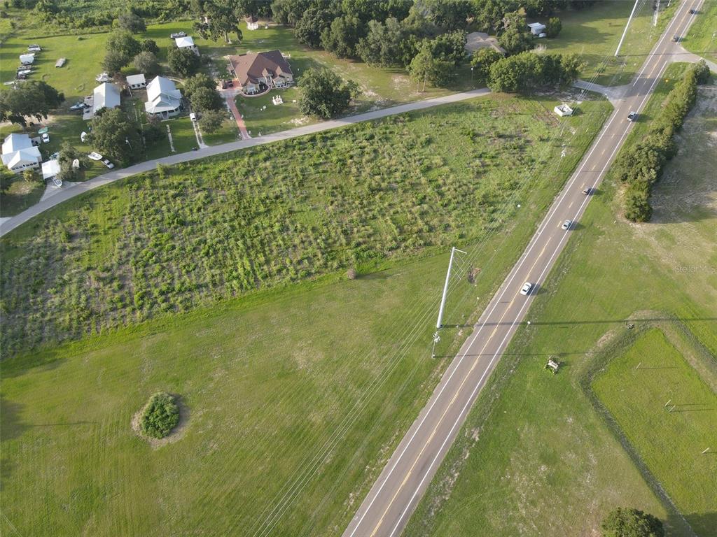 An aerial view shows a vacant, grassy lot bordered by a road and nearby houses — 104 SCENIC HIGHWAY, HAINES CITY, FL