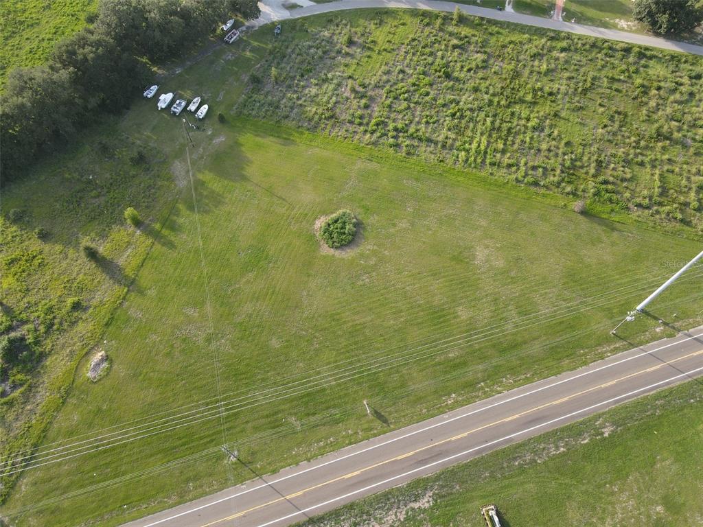 An aerial view shows a grassy, triangular vacant lot bordered by a road and trees — 104 SCENIC HIGHWAY, HAINES CITY, FL