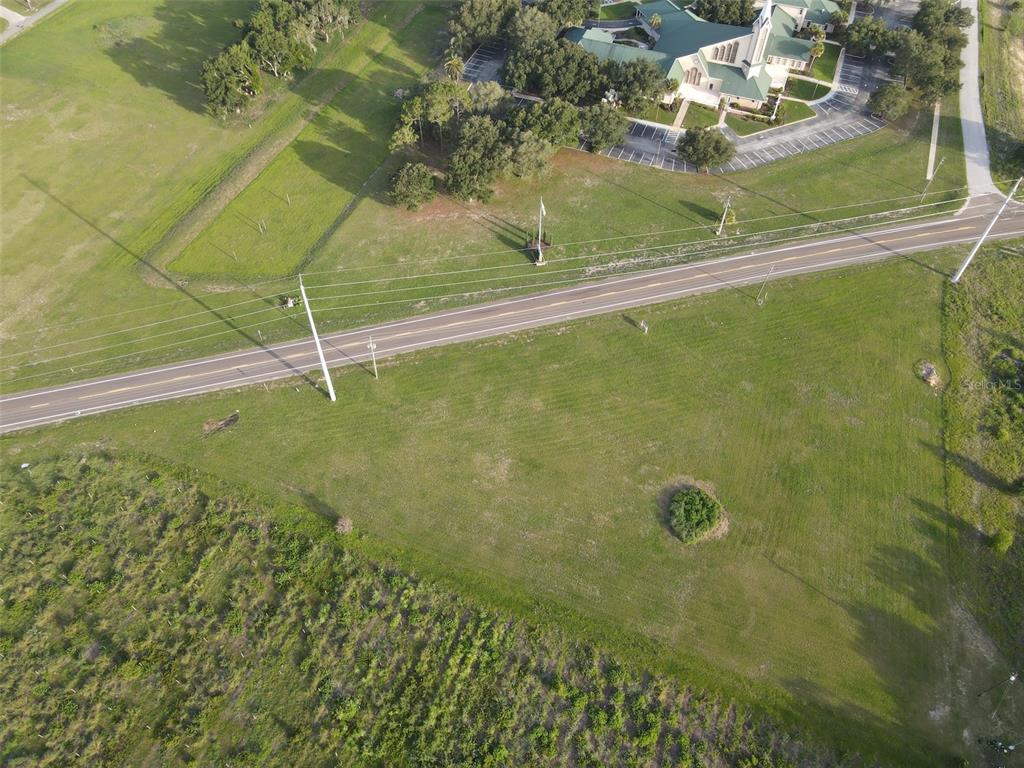 An aerial view shows a large, grassy vacant lot bordering a road near a church — 104 SCENIC HIGHWAY, HAINES CITY, FL