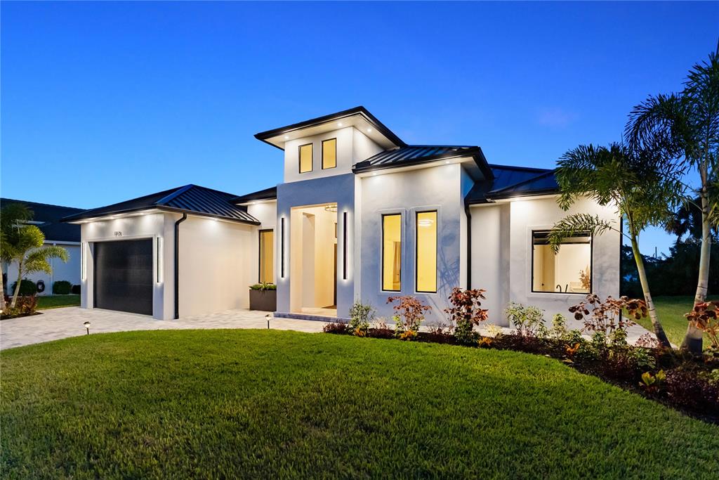 A modern single-story house with a white stucco exterior, dark metal roof, and attached garage — 13125 IRWIN DRIVE, PORT CHARLOTTE, FL