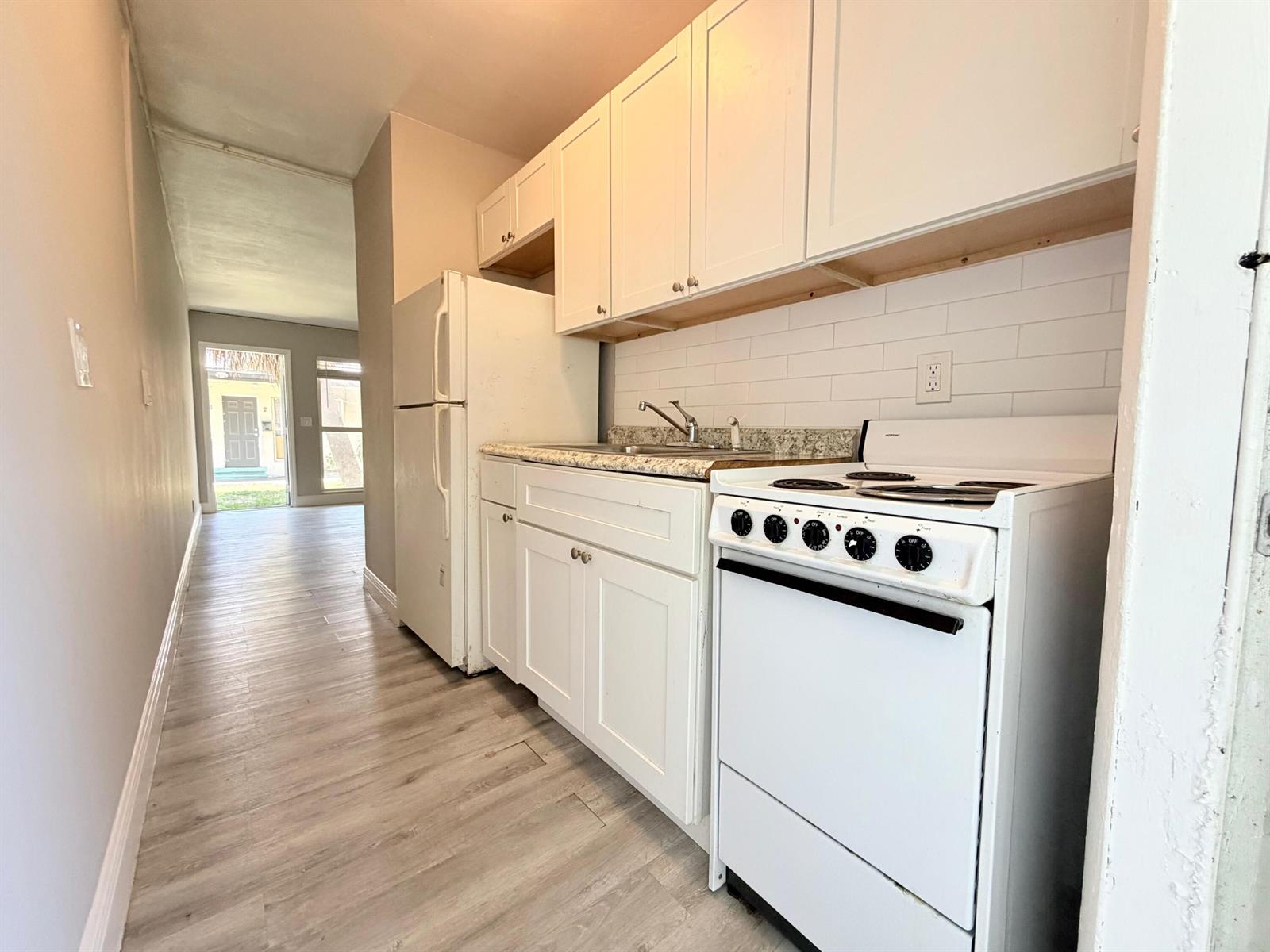 A galley-style kitchen features white cabinets, a white stove, a refrigerator, and light wood flooring — 809 2nd Street # 2, West Palm Beach FL 33401, WEST PALM BEACH, FL