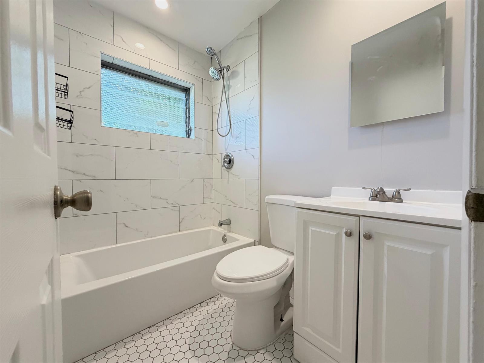 A bathroom features a white bathtub with marble-look tile walls, a toilet, and a vanity — 809 2nd Street # 2, West Palm Beach FL 33401, WEST PALM BEACH, FL