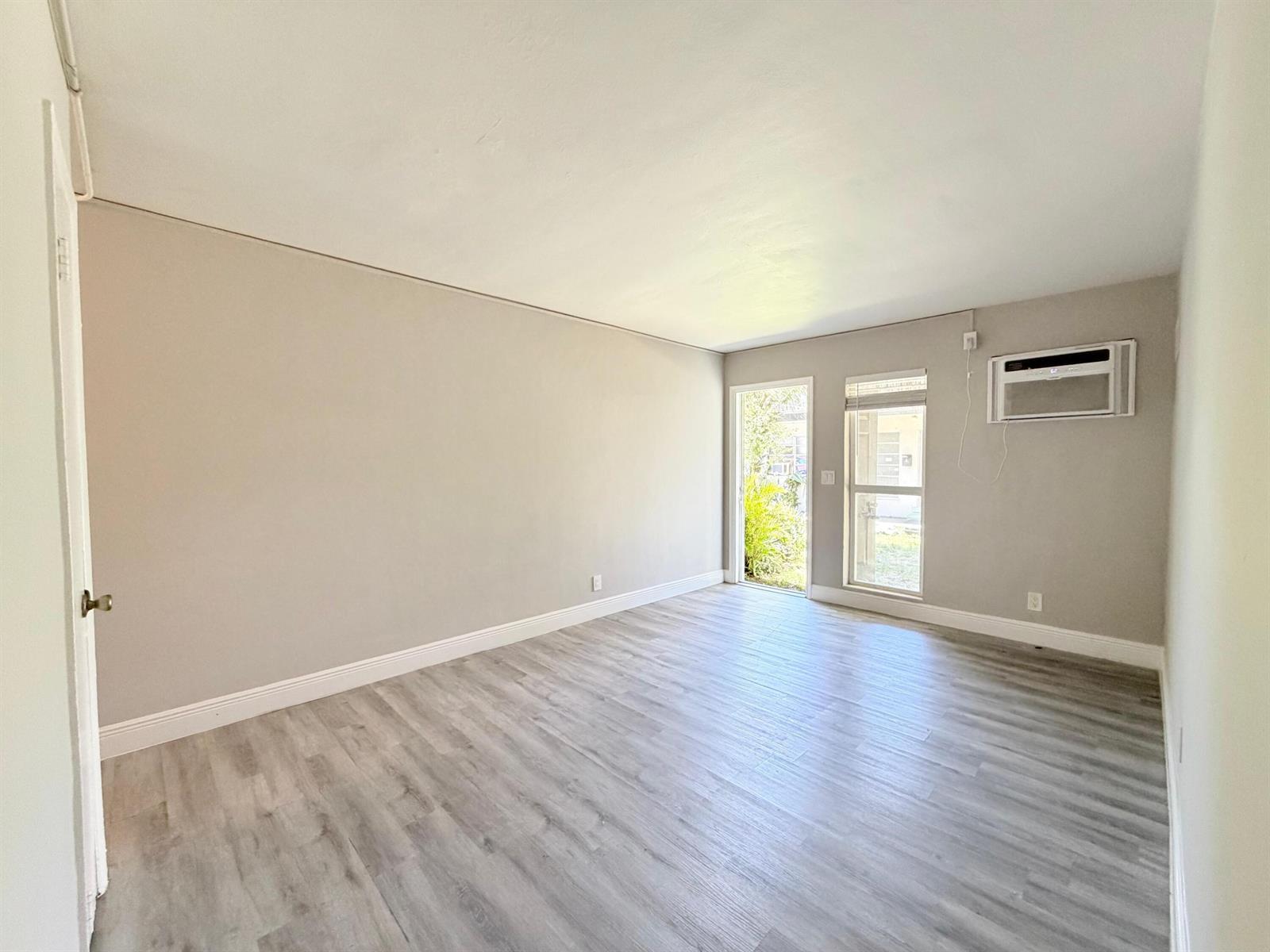 An empty room features light gray walls, wood-look flooring, a window, and a glass door — 809 2nd Street # 2, West Palm Beach FL 33401, WEST PALM BEACH, FL
