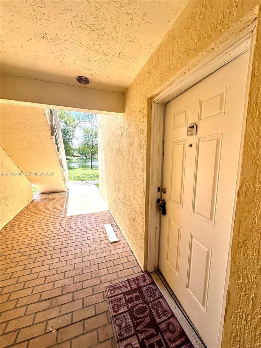 A white front door with a lockbox opens onto a brick walkway overlooking a pond — 3630 N 56th Ave # 310, Hollywood FL 33021, HOLLYWOOD, FL