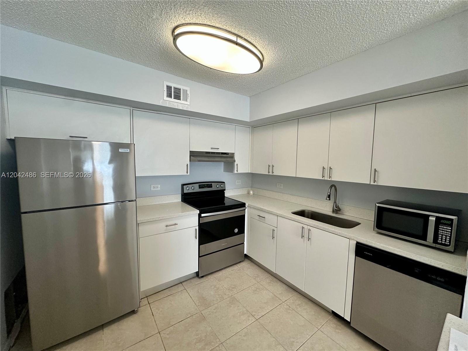 A kitchen features white cabinets, stainless steel appliances, light countertops, and beige tile flooring — 3630 N 56th Ave # 310, Hollywood FL 33021, HOLLYWOOD, FL