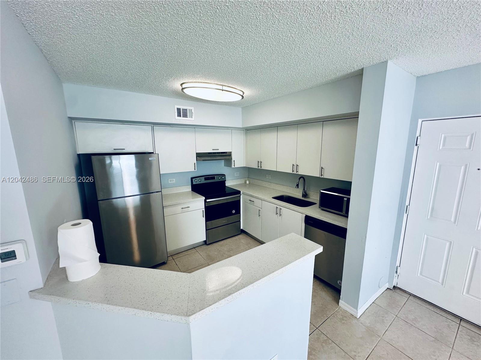 A kitchen features white cabinets, stainless steel appliances, and a light-colored stone countertop peninsula — 3630 N 56th Ave # 310, Hollywood FL 33021, HOLLYWOOD, FL