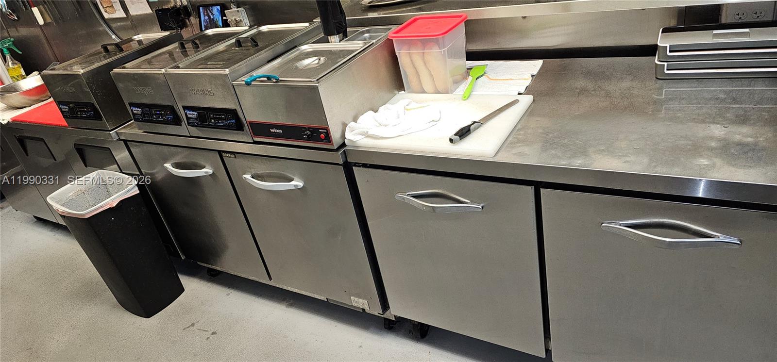 A commercial kitchen features stainless steel countertops, under-counter refrigeration units, and various food preparation equipment — Collins Ave, Sunny Isles Beach FL 33160, SUNNY ISLES BEACH, FL
