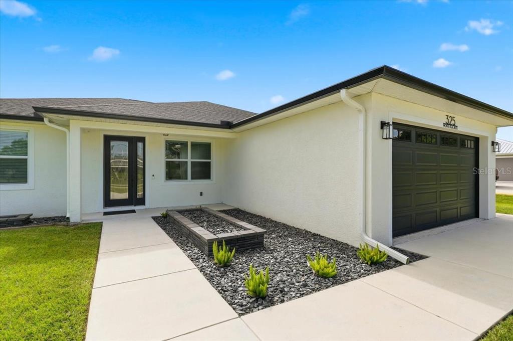 The exterior of a house features a dark garage door, a front entrance, and a planter — 325 MONTE REAL BOULEVARD, SEBRING, FL