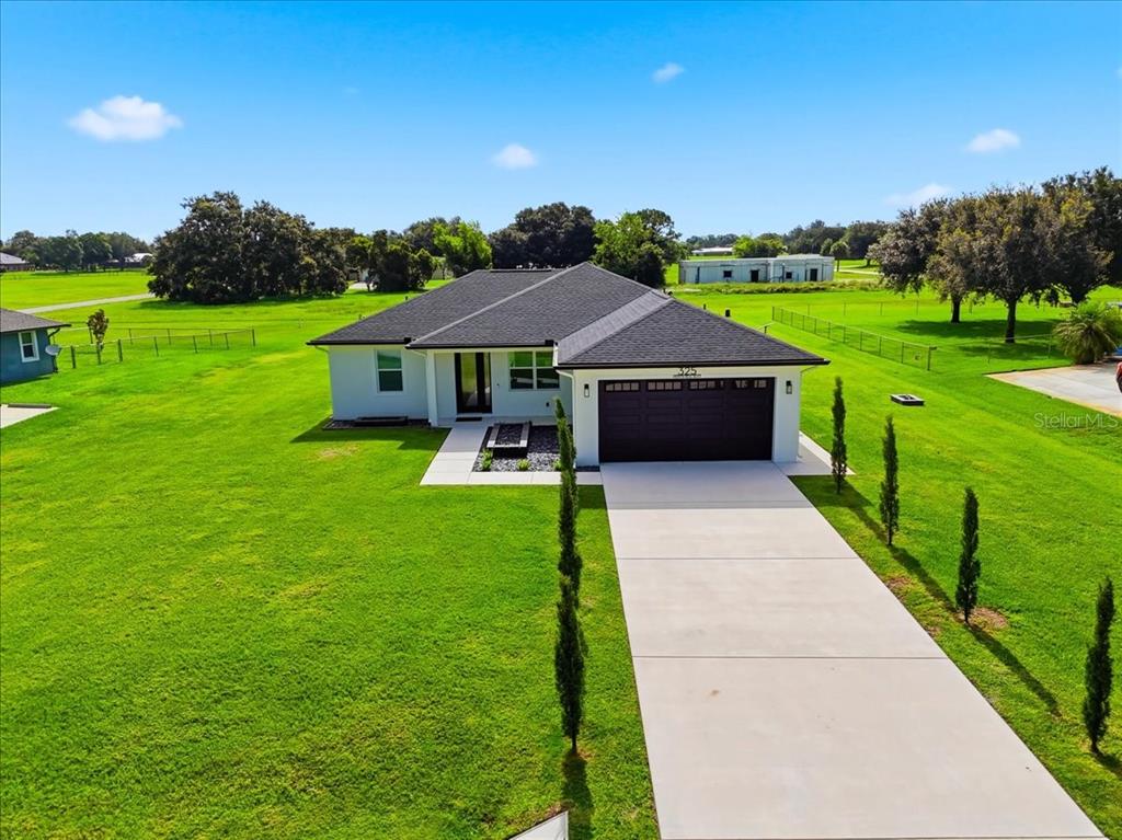 An aerial view shows a modern single-story house with a dark roof and concrete driveway — 325 MONTE REAL BOULEVARD, SEBRING, FL