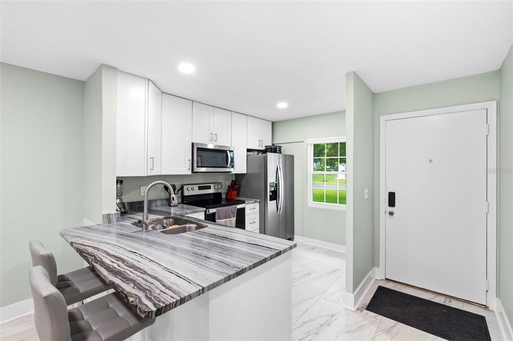 A kitchen features white cabinets, a stone-patterned island countertop, stainless steel appliances, and tile flooring — 4651 LAKE VILLA DRIVE, CLEARWATER, FL