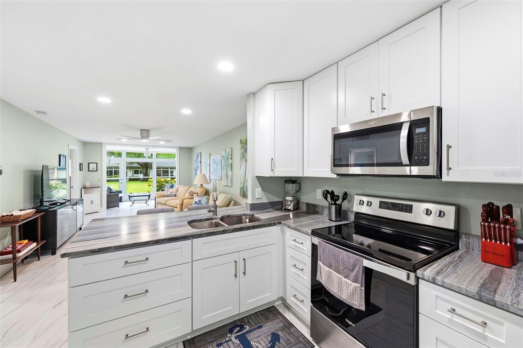 A kitchen with white cabinets, grey stone countertops, and stainless steel appliances overlooks a living area — 4651 LAKE VILLA DRIVE, CLEARWATER, FL