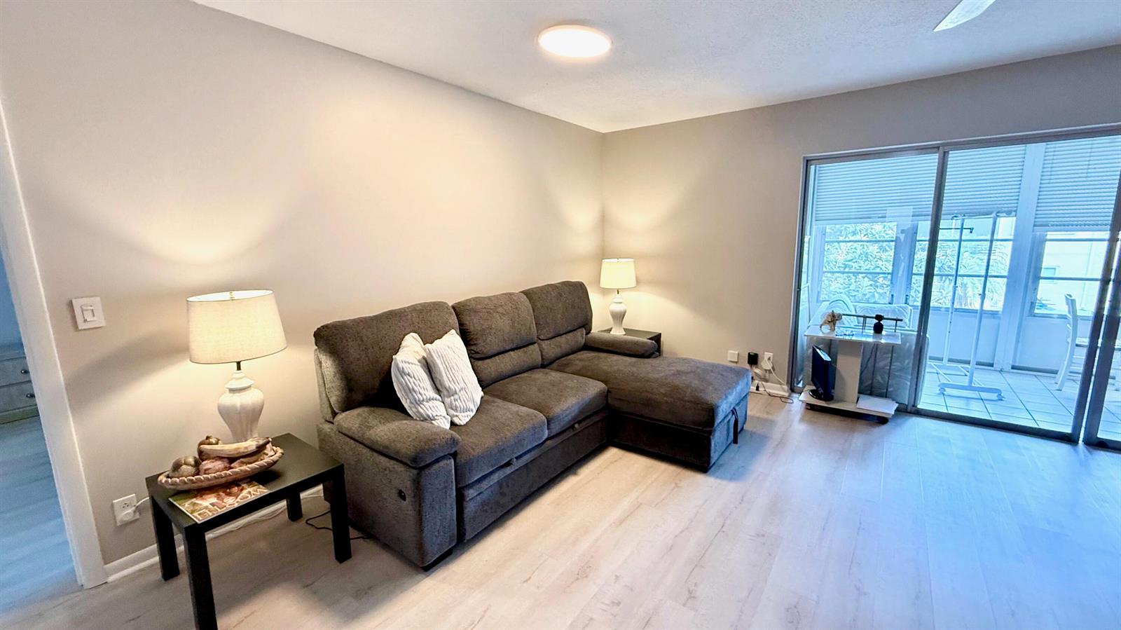 A living room features a gray sectional sofa, two side tables with lamps, and sliding doors — 705 Lori Drive # 209, Palm Springs FL 33461, PALM SPRINGS, FL