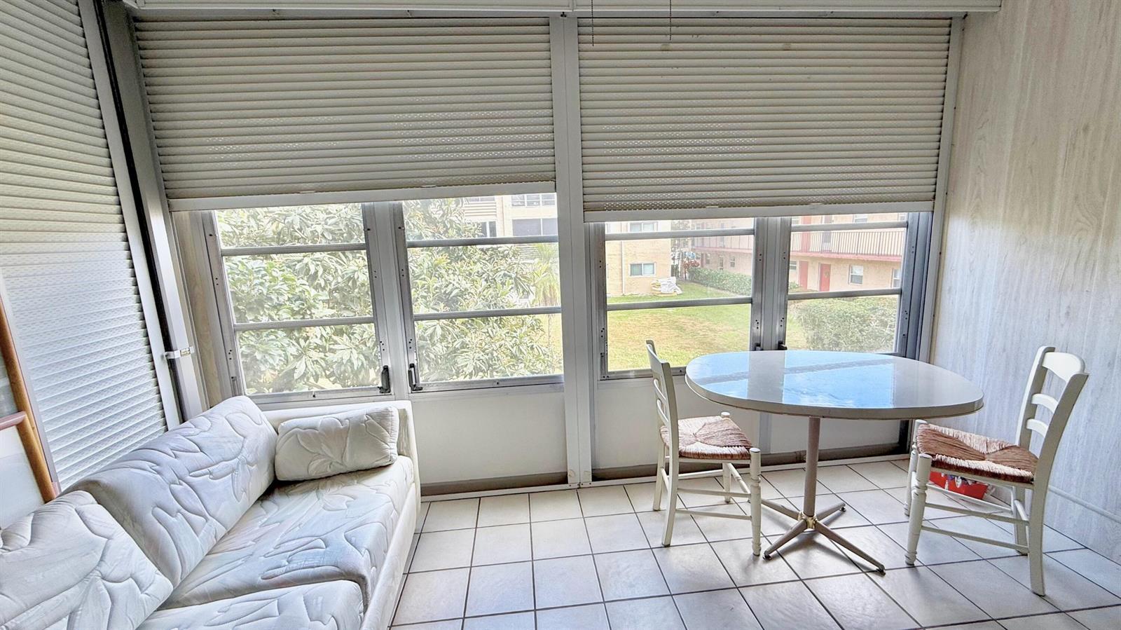 A sunroom features tile flooring, a white sofa, a round table, and two wooden chairs — 705 Lori Drive # 209, Palm Springs FL 33461, PALM SPRINGS, FL