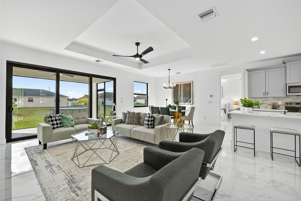 A bright, open-concept living room and kitchen featuring white marble floors and a tray ceiling — 3205 12TH STREET SW, LEHIGH ACRES, FL
