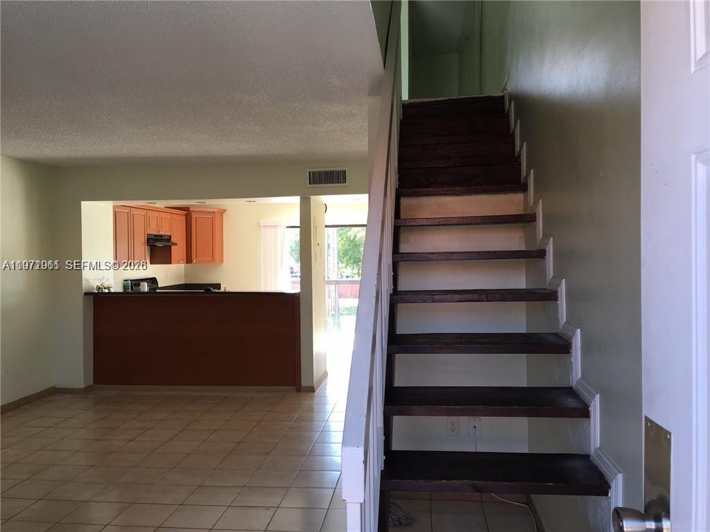 An interior view shows a staircase with dark wood treads next to a tiled kitchen — 2162 W 60th St # 14208, Hialeah FL 33016, HIALEAH, FL