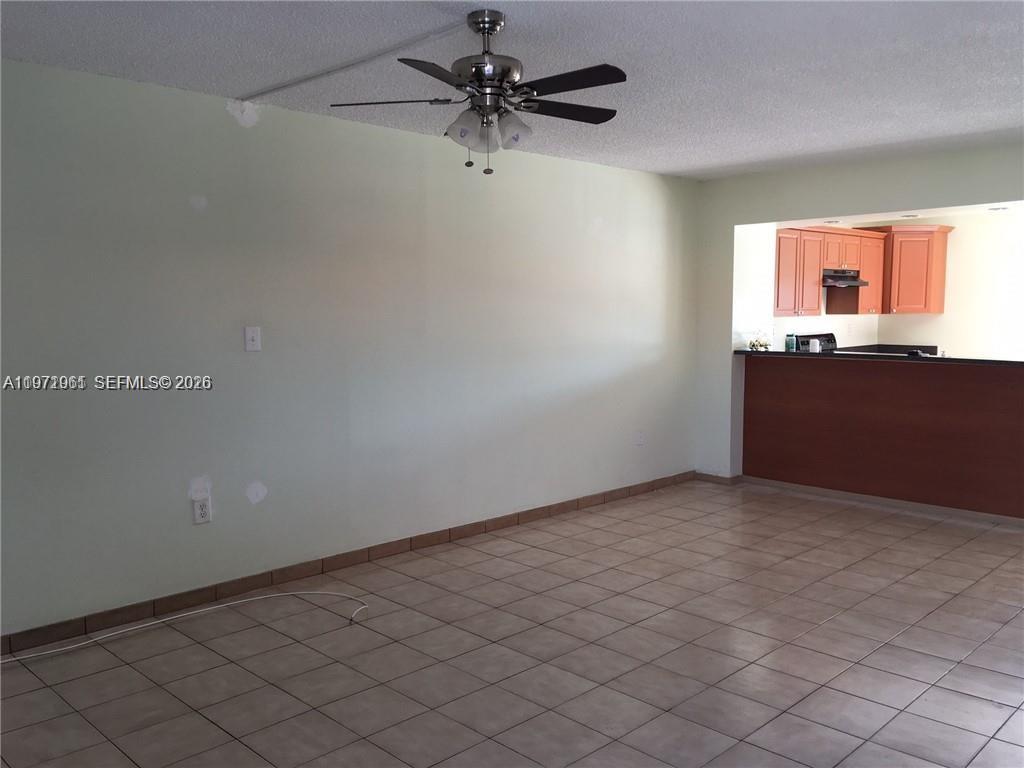 An empty room features light-colored walls, tiled flooring, a ceiling fan, and a kitchen pass-through — 2162 W 60th St # 14208, Hialeah FL 33016, HIALEAH, FL