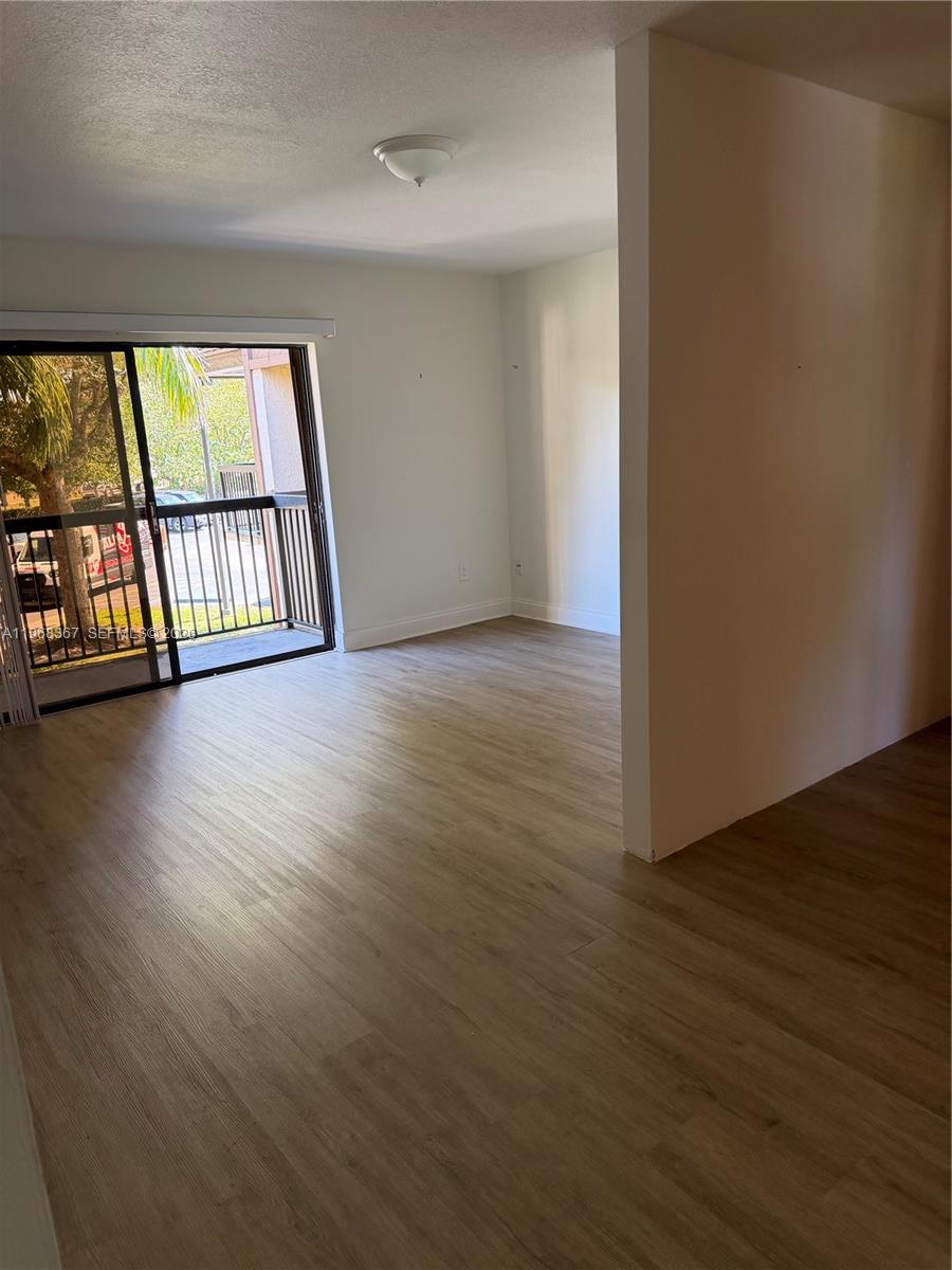 An empty room features light wood-look flooring, white walls, and a sliding glass balcony door — 7925 SW 86th St # 923, Miami FL 33143, MIAMI, FL