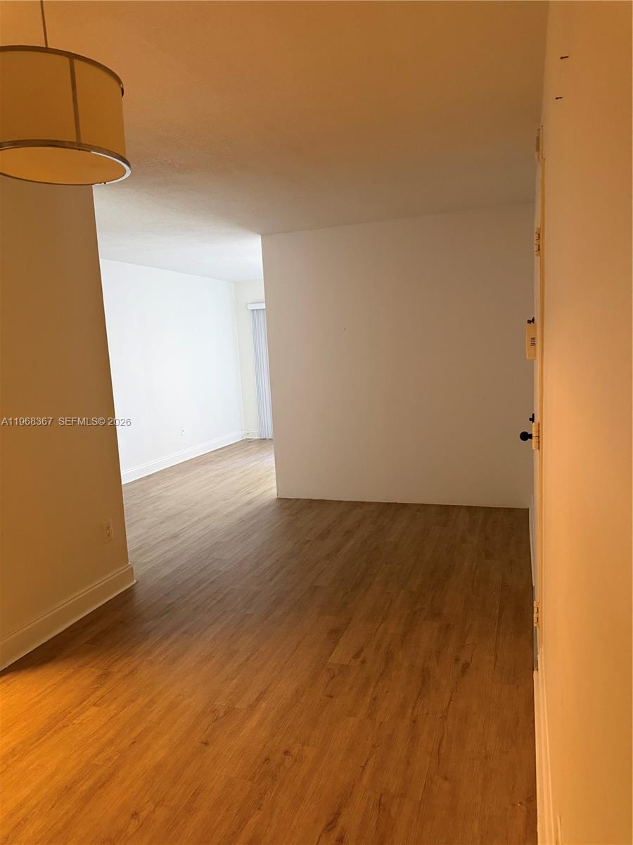 An empty room features light wood-look flooring, white walls, and a hanging pendant light — 7925 SW 86th St # 923, Miami FL 33143, MIAMI, FL