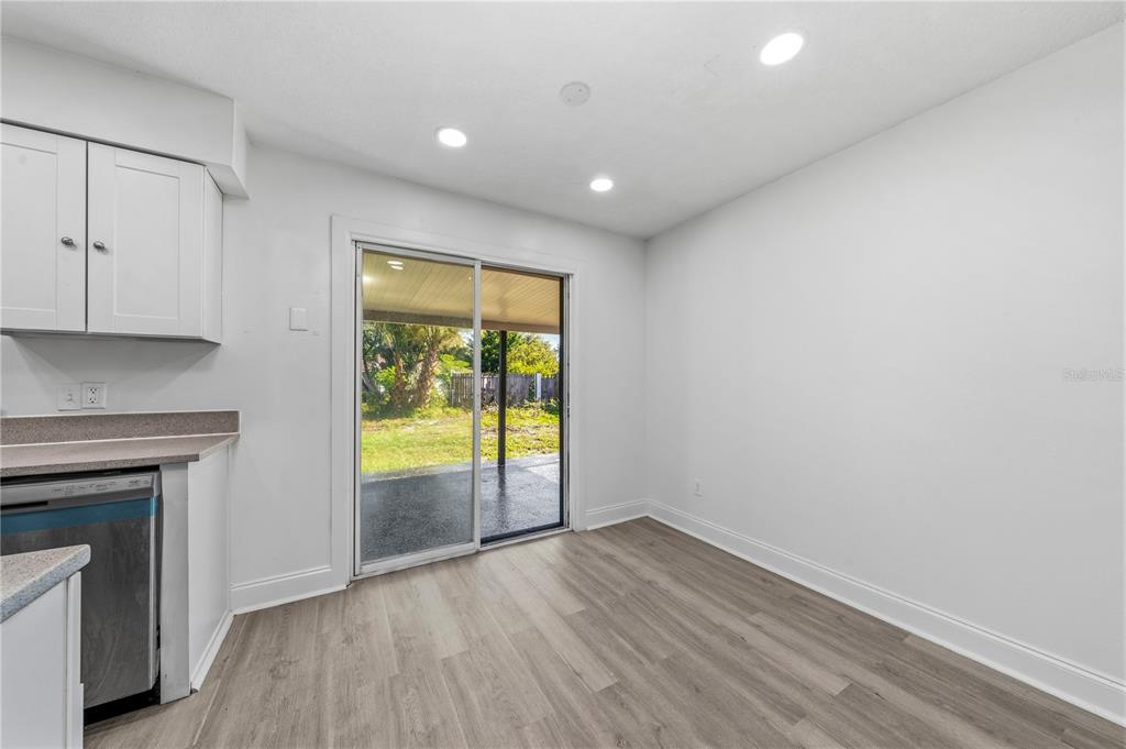 A kitchen dining area with white cabinets, light wood flooring, and a sliding glass door — 618 JUPITER WAY, CASSELBERRY, FL