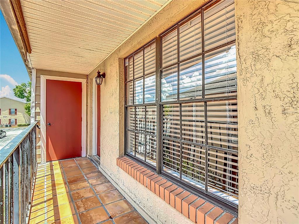 A balcony with tiled flooring, a red door, and a large window with blinds — 21032 VOYAGER BLVD UNIT 8, LAND O LAKES, FL
