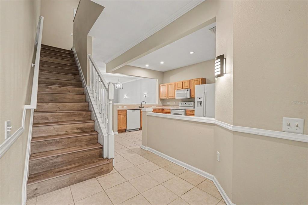 A staircase with wood steps sits beside a kitchen featuring light wood cabinets — 26533 CASTLEVIEW WAY, WESLEY CHAPEL, FL