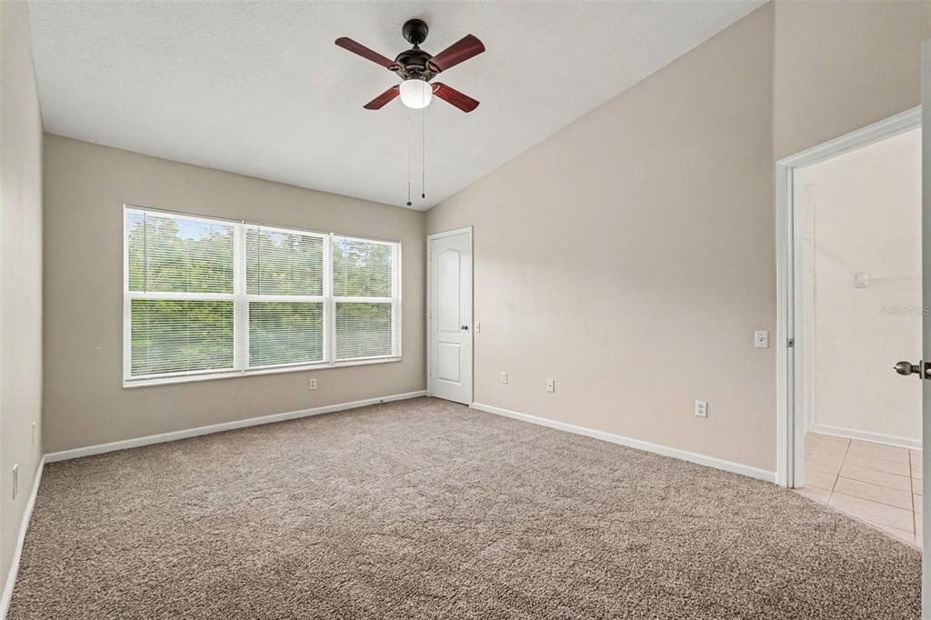 A carpeted bedroom features a vaulted ceiling, a ceiling fan, and a window with blinds — 26533 CASTLEVIEW WAY, WESLEY CHAPEL, FL