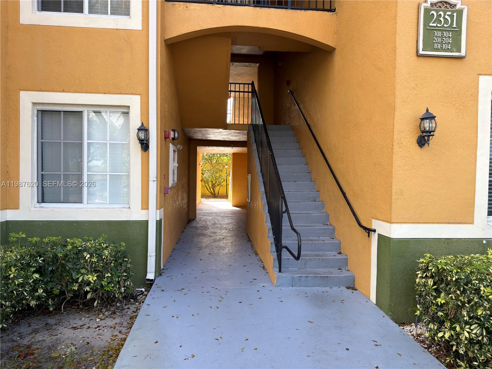 An exterior view of an apartment building entrance with stairs leading to upper levels — 2351 W Preserve Way # 104, Miramar FL 33025, MIRAMAR, FL