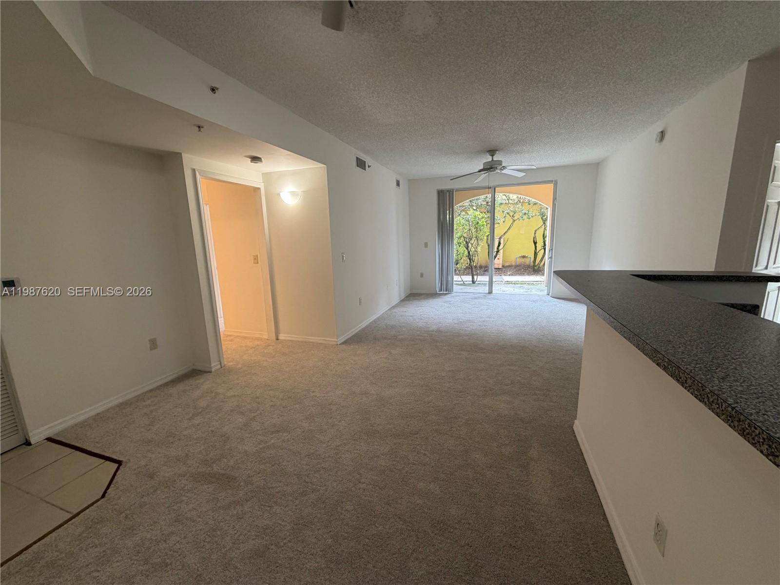 An empty living room features beige carpeting, a ceiling fan, and a sliding glass door — 2351 W Preserve Way # 104, Miramar FL 33025, MIRAMAR, FL