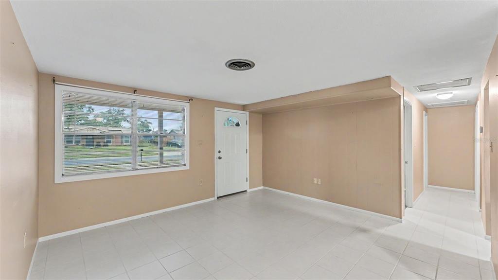 A living room with beige walls, white tile flooring, a window with blinds, and a door — 2126 SMITHFIELD PLACE, LAKELAND, FL