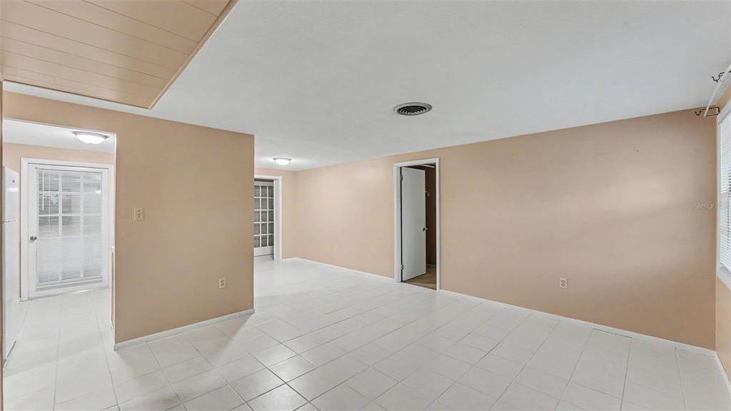 An interior room with beige walls, white tile flooring, and multiple doorways — 2126 SMITHFIELD PLACE, LAKELAND, FL