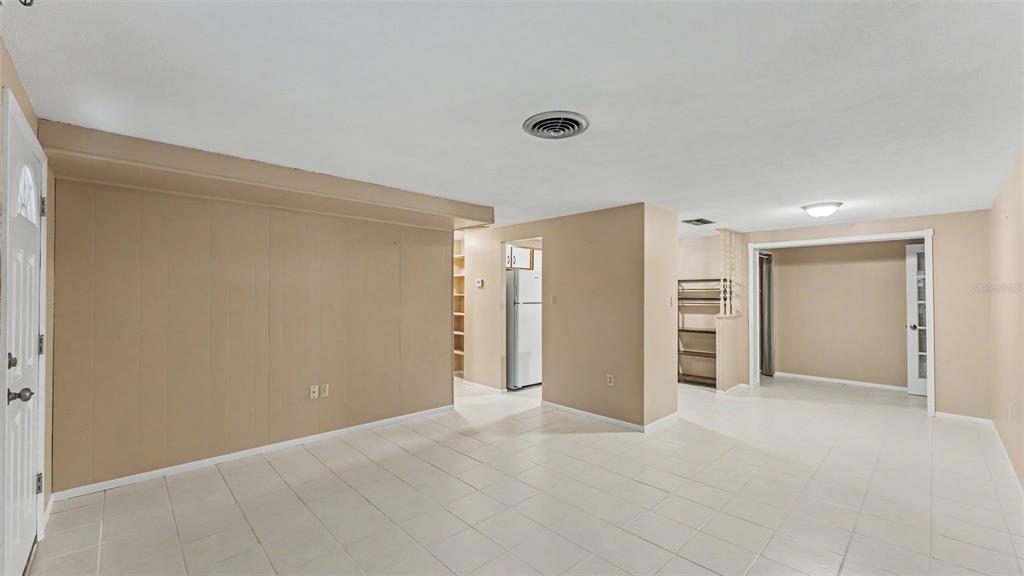 An interior view of a room with beige paneled walls, white tile flooring, and a refrigerator — 2126 SMITHFIELD PLACE, LAKELAND, FL