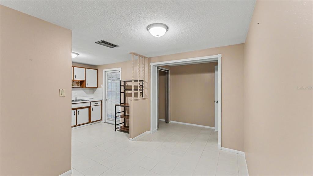 A kitchen with white cabinets and tile flooring opens into an adjacent room with beige walls — 2126 SMITHFIELD PLACE, LAKELAND, FL