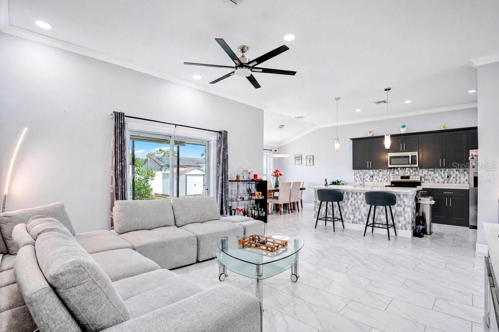 An open-concept living room and kitchen with light tile floors and dark cabinetry — 2412 AINSWORTH AVENUE, DELTONA, FL