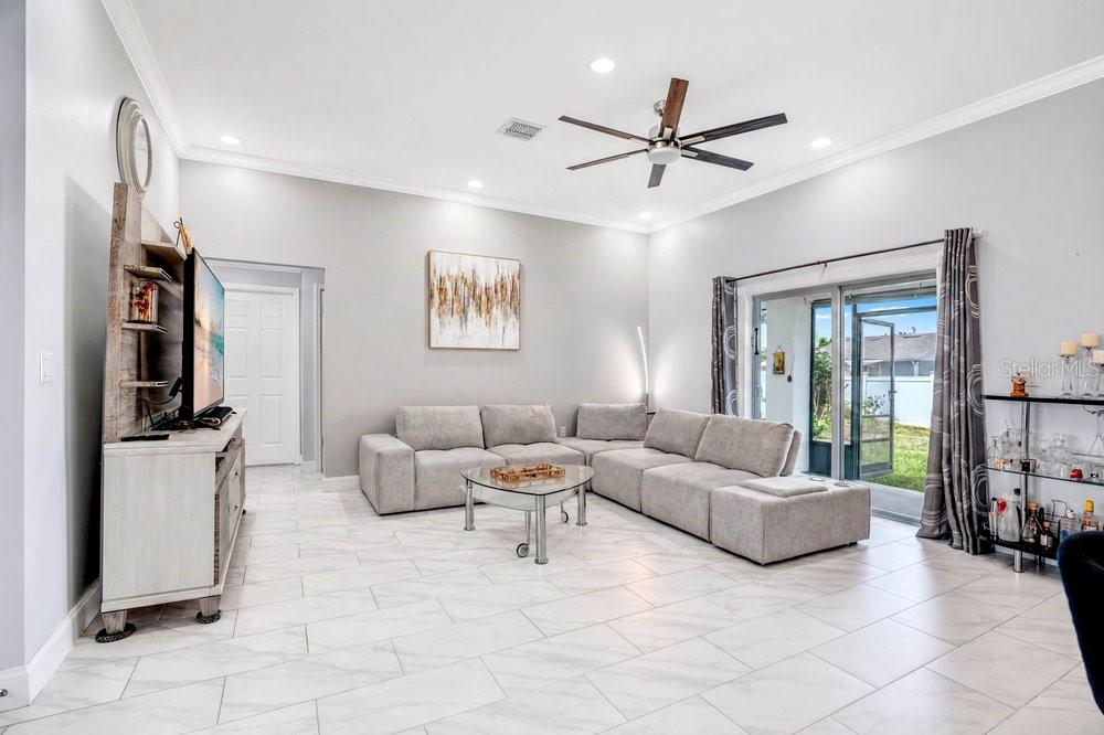 A living room with light gray walls, a sectional sofa, tile floors, and sliding glass doors — 2412 AINSWORTH AVENUE, DELTONA, FL