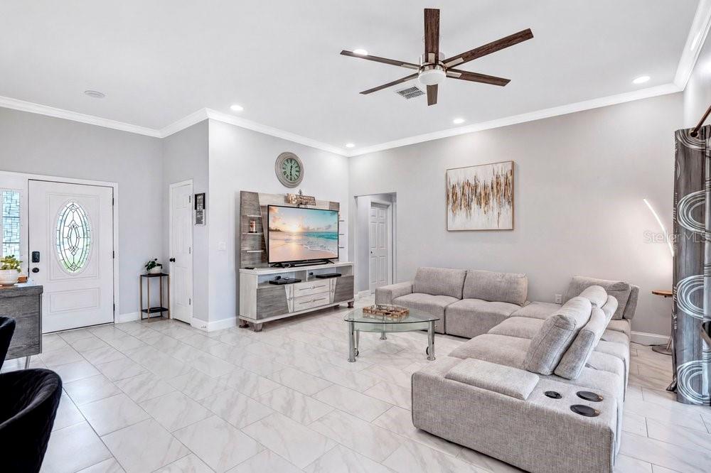 A living room features light tile floors, a sectional sofa, and a wall-mounted television — 2412 AINSWORTH AVENUE, DELTONA, FL