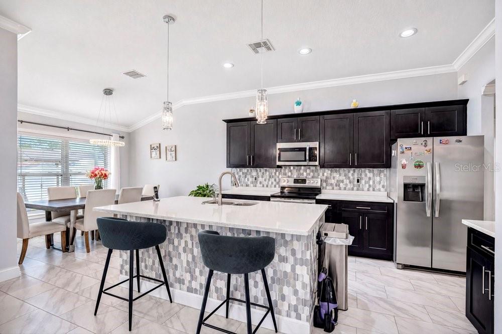 A kitchen features dark cabinets, a white quartz island with bar stools, and tiled flooring — 2412 AINSWORTH AVENUE, DELTONA, FL