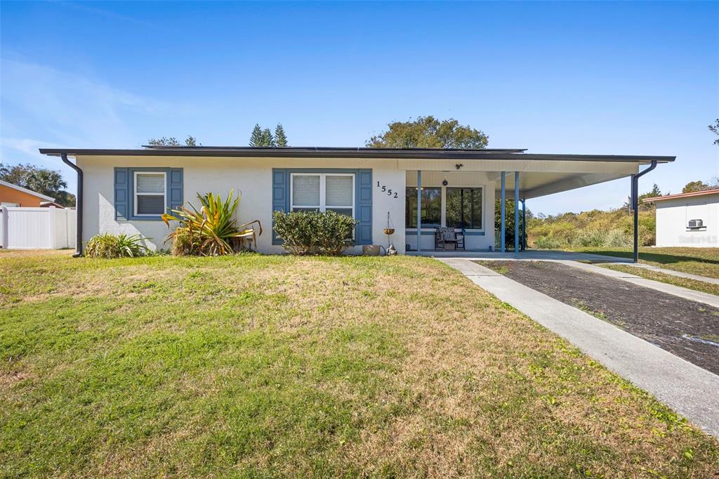 A single-story house with a white stucco exterior, blue shutters, and an attached carport — 1552 ZINNIA DRIVE, DELTONA, FL