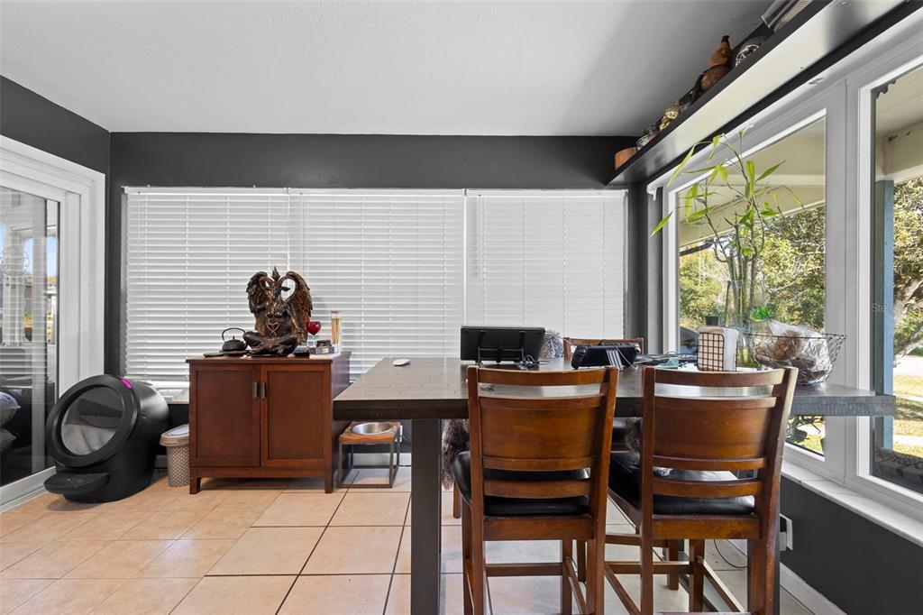 A dining area features a dark wood table, matching chairs, tile flooring, and large windows — 1552 ZINNIA DRIVE, DELTONA, FL