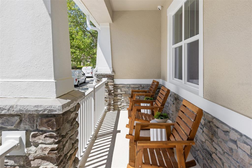 A covered front porch features stone accents, white railings, and two wooden rocking chairs — 233 SPINDLE PALM COVE, WINTER SPRINGS, FL