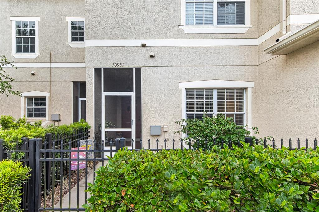 The exterior of a multi-story stucco townhouse features a screened entryway and a black fence — 10951 WINTER CREST DRIVE, RIVERVIEW, FL