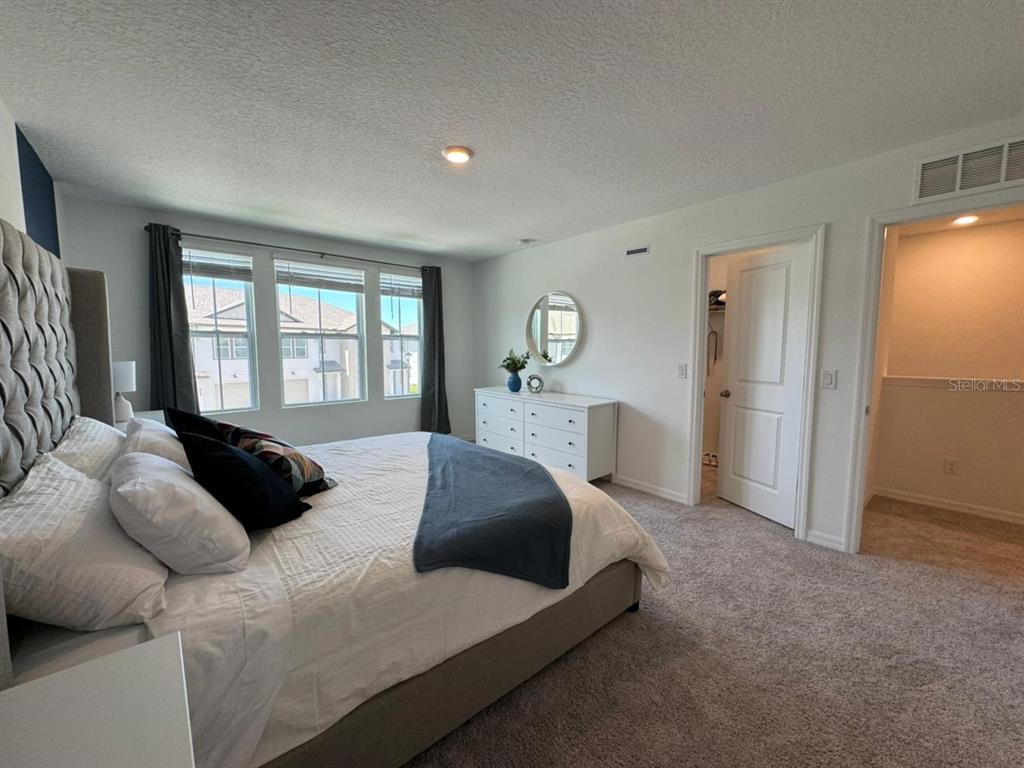 A bedroom features a tufted headboard, white dresser, carpeted flooring, and two doorways — 661 LONGBOAT DRIVE, DAVENPORT, FL